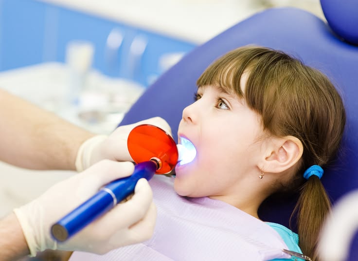 little girl with open mouth receiving dental filling drying proc