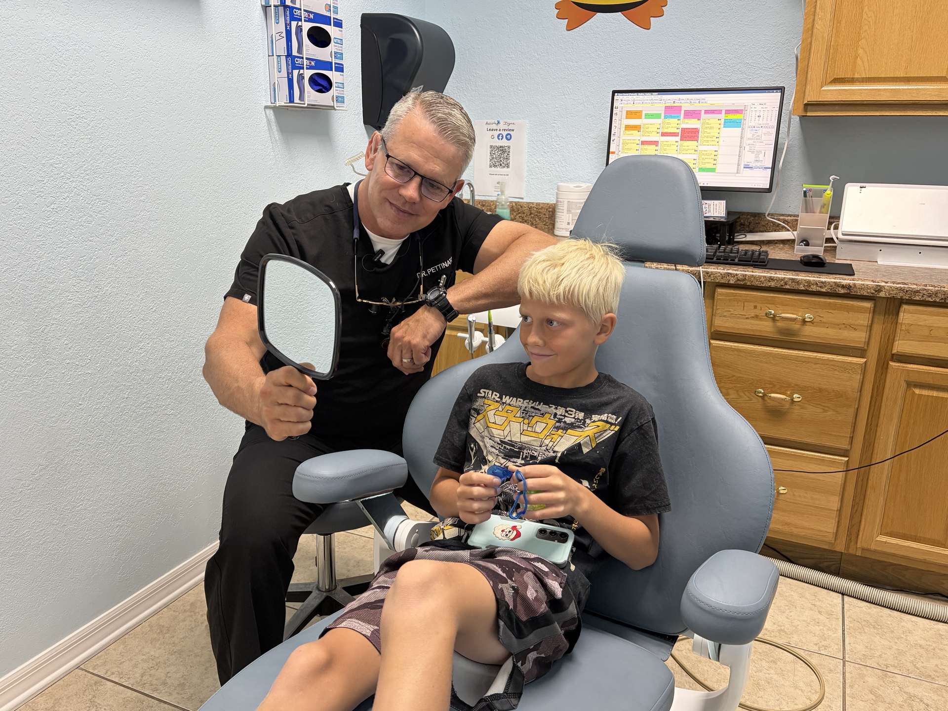 Dr. Pettinato holding a mirror so a young patient can see his smile at Cool Kid Dental