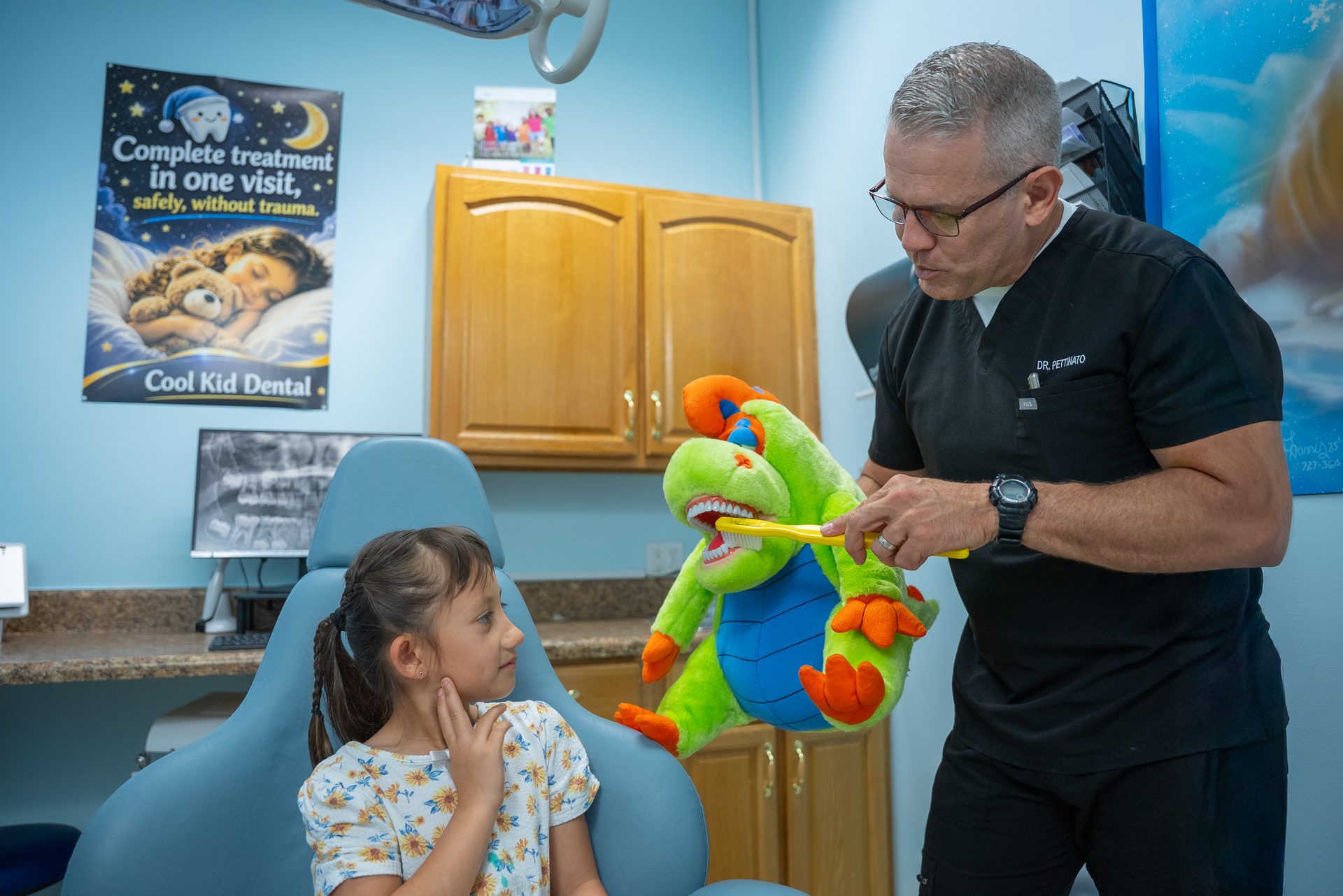 Dr. Pettinato showing a young patient how to brush with a dinosaur puppet at Cool Kid Dental in North Port
