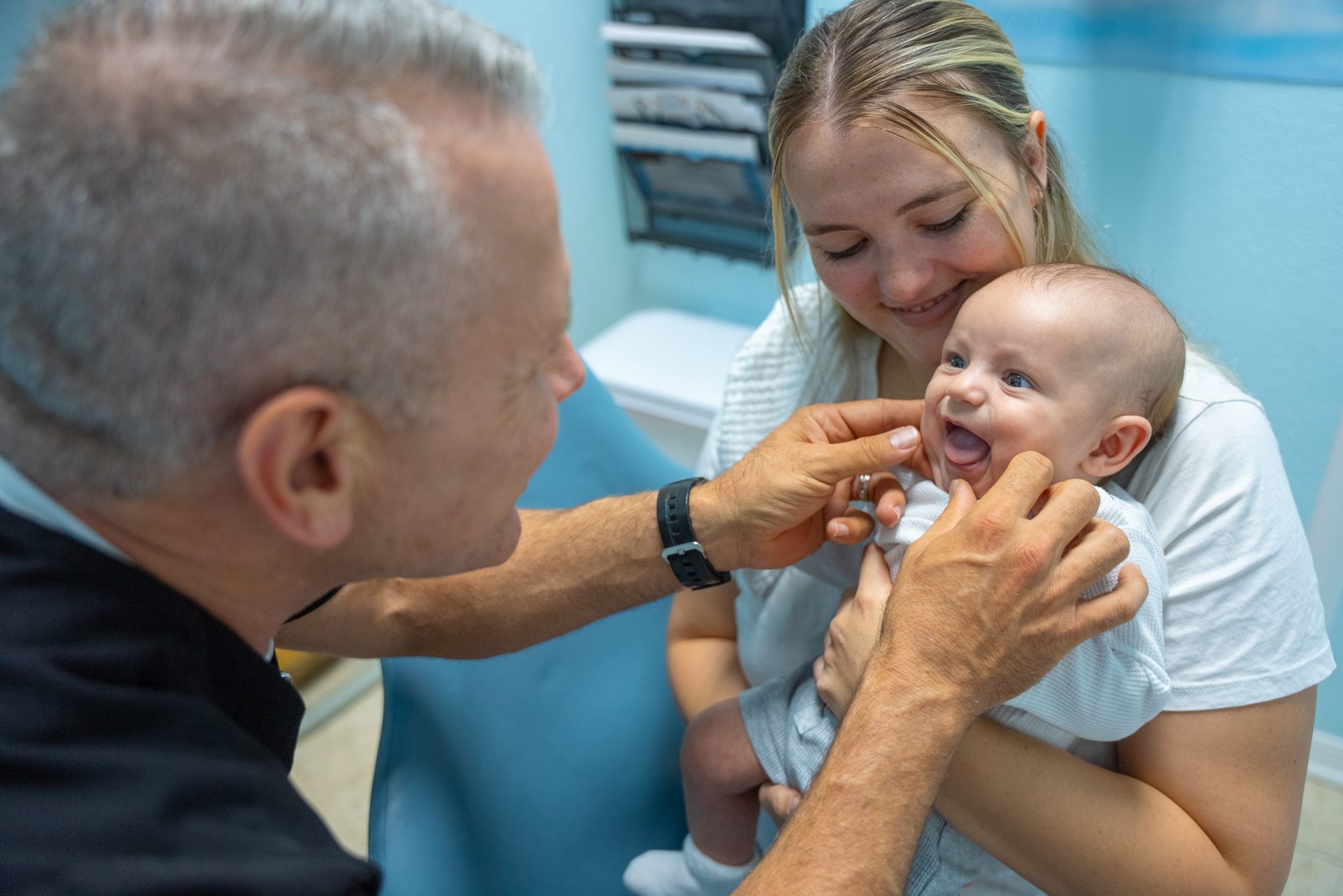 Dr. Pettinato gently examining a smiling baby held by her mom at Cool Kid Dental