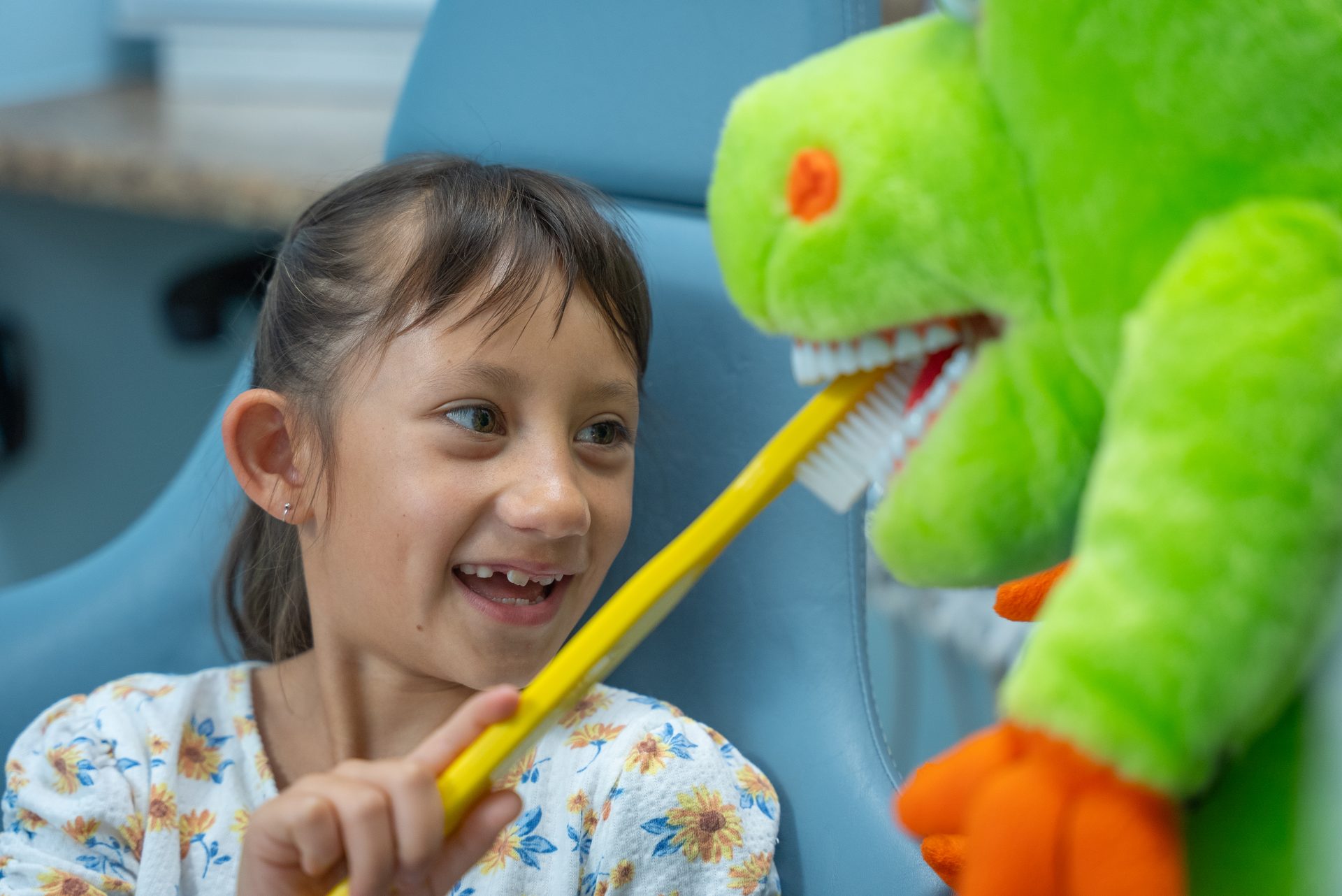 Smiling girl brushing the teeth of a dinosaur puppet at Cool Kid Dental in North Port